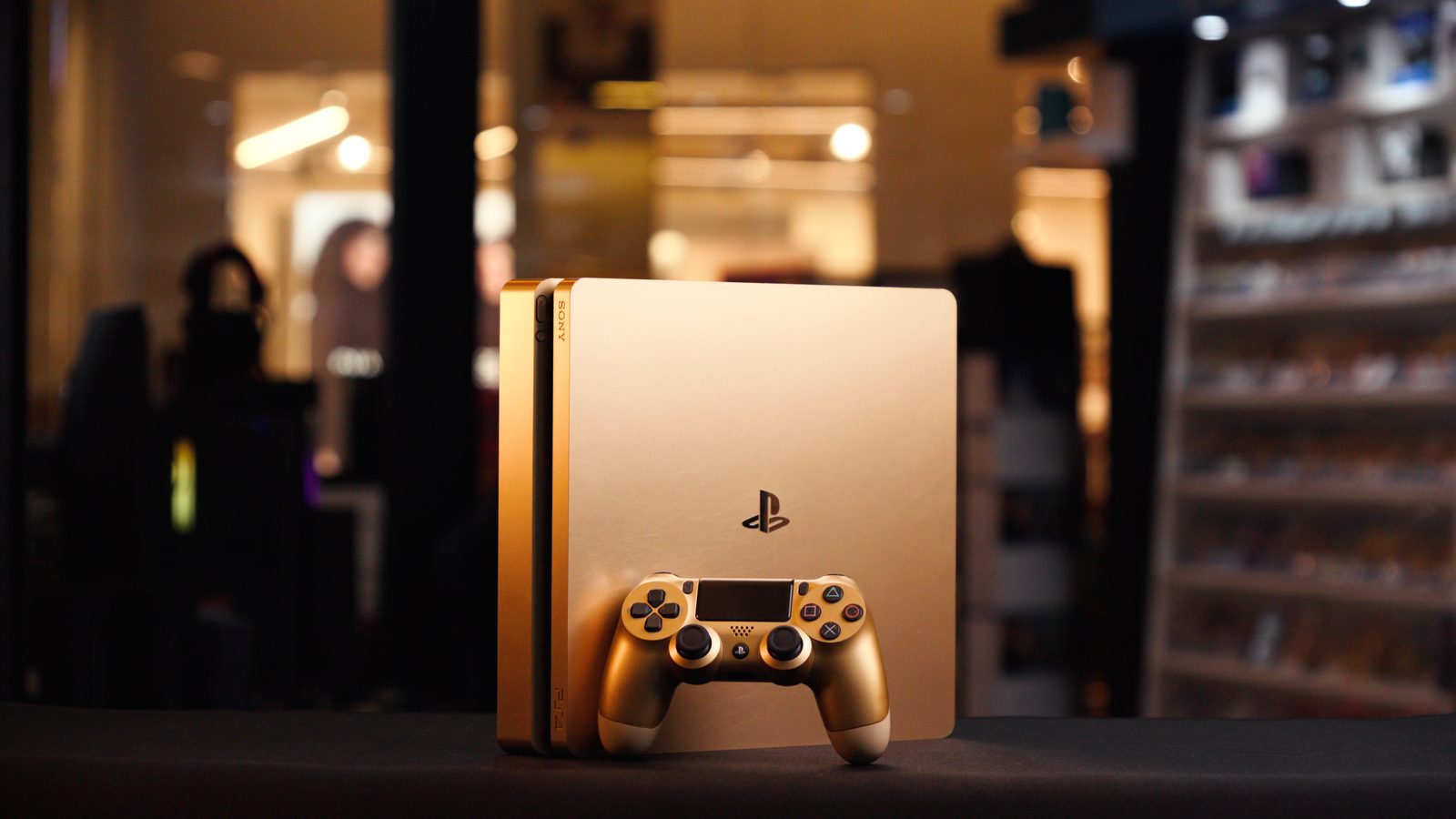 PlayStation 4 Slim dourado usado, com controle dourado, no balcão de uma loja Game Mania