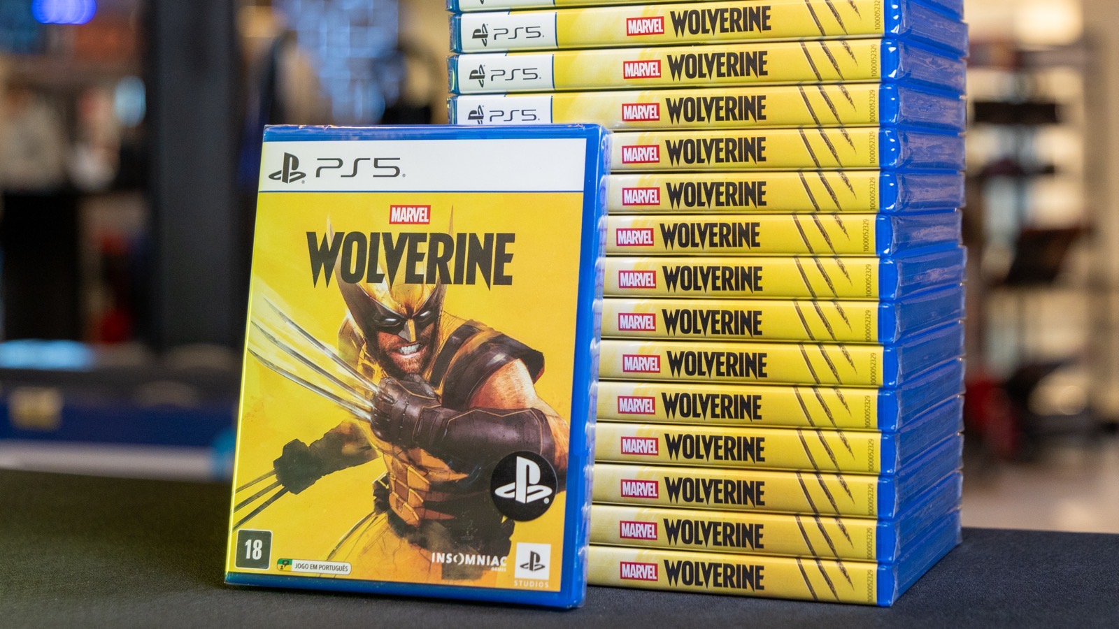 Unidade de Marvel's Wolverine em destaque com pilha de cópias do jogo ao fundo, em uma loja Game Mania